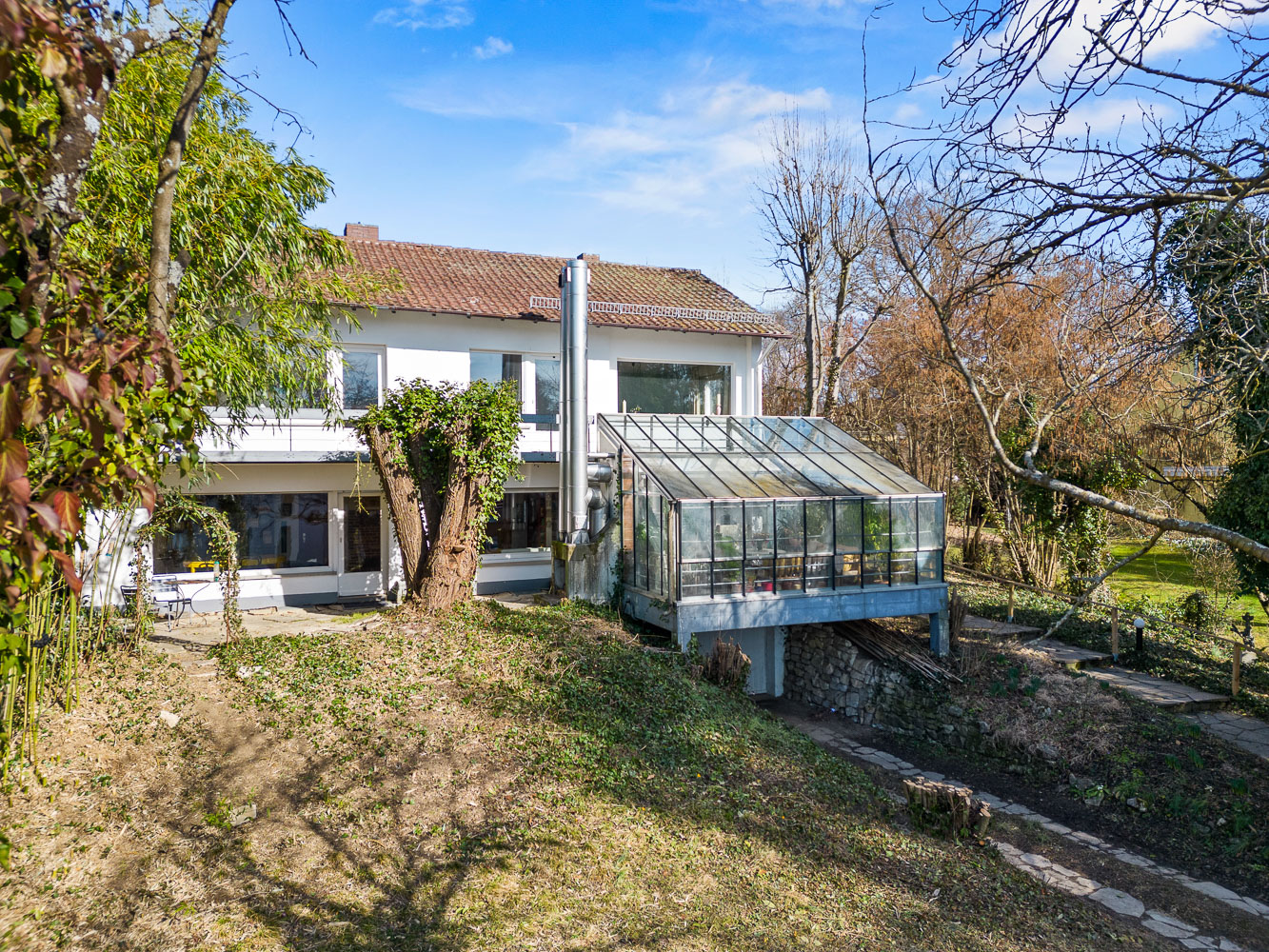 Haus mit Wintergarten und großem Garten mit Baumbestand im Frühling